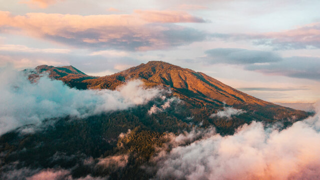 Aerial view of lush mountain slopes partially covered by thick clouds during a golden sunset in Kecamatan Pujon, Jawa Timur, Indonesia.