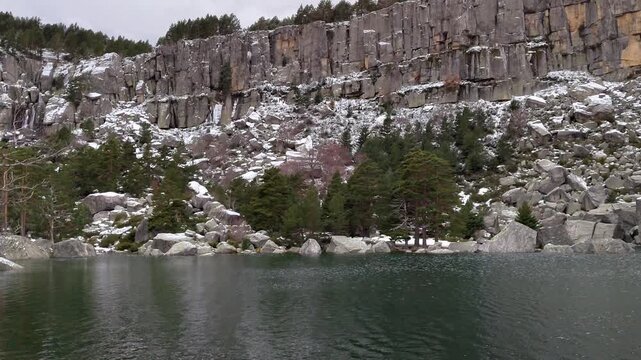 Laguna Negra in Soria, Spain. Winter scene of the lake with rocky cliff snow-dusted trees reflected in calm water under cloudy sky