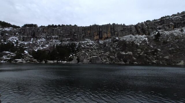 Panoramic winter view of Laguna Negra in Soria, Castilla y Leon, Spain. Snowed cliff and trees. Scattered clouds in the sky.