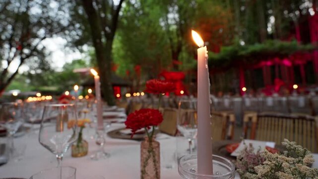 Outdoor banquet table set with taper candles red carnations wine glasses and gold chairs
