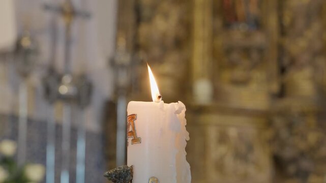 Lit paschal candle with alpha letter and dripping wax before a gilded altarpiece and crucifix