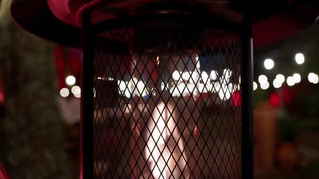 Outdoor gas patio heater with mesh guard glowing on a cafe terrace at night with string lights
