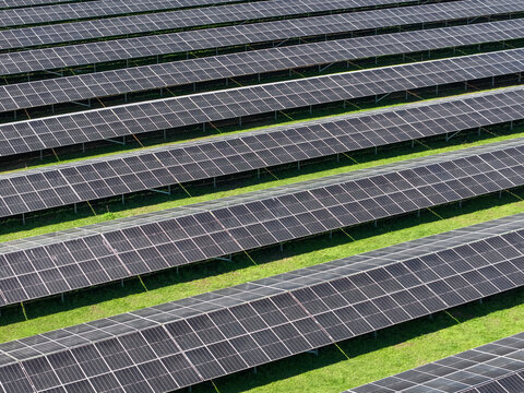 Aerial view of rows of photovoltaic solar panels arranged in neat lines over green grass at a solar farm in The Basin, Victoria, Australia.