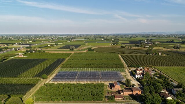 Aerial view of solar panels installed in agricultural fields surrounded by orchards and vineyards near Faenza, Emilia-Romagna, Italy.