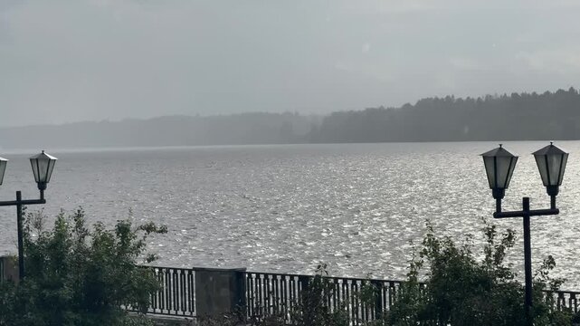 Gloomy rainy weather over a dark river and dense forest, heavy clouds, drizzle, mist, wet trees, somber mood, candid authentic life moment in nature today very real and cold.