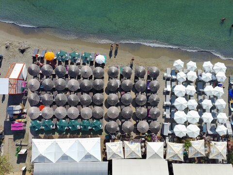 Aerial view of the beach with organized rows of sun loungers and umbrellas along the turquoise shoreline in Katarinies Paralia, Greece.