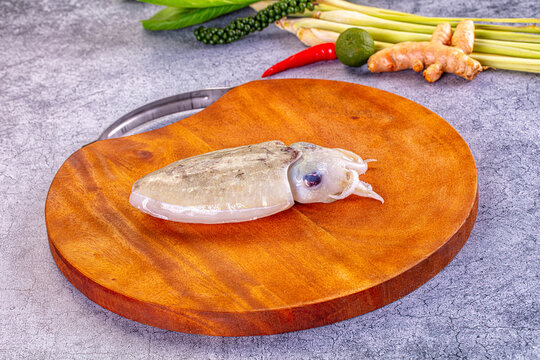 Fresh cuttlefish on wooden cutting board with lemongrass, ginger, chili and lime in background for seafood cooking preparation