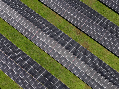 Aerial view of solar panels arranged in parallel rows across a green grassy field in The Basin, Victoria, Australia.
