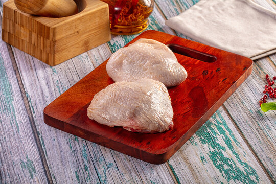 Raw chicken thighs on wooden cutting board with spice jar and peppercorns on rustic painted wood surface