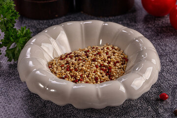 Raw tricolor quinoa grains in ceramic bowl with parsley and red peppers on dark textured surface