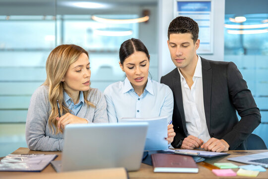 Business executives reviewing financial reports and corporate strategy together on computer screen in boardroom.