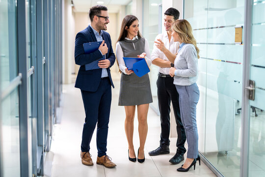 Young colleagues smiling and chatting together in corporate office corridor