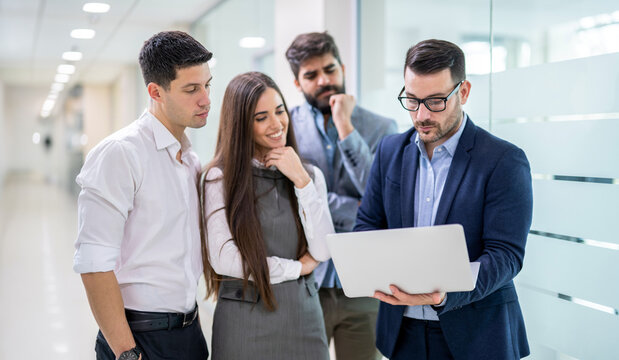 Businessman showing laptop screen to group of attentive colleagues standing in office