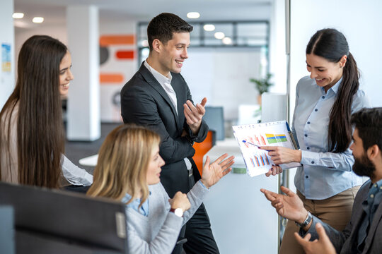 Businesswoman presenting sales report charts to colleagues gathered in modern office