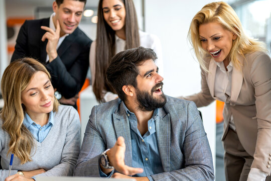Happy business team celebrating successful project results around desk in office