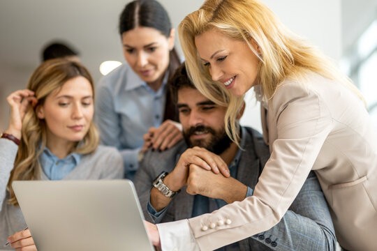 Business team gathered around computer discussing strategy and working on laptop in modern office