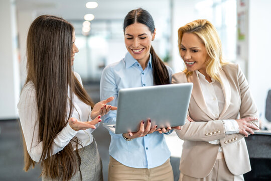 Three smiling businesswomen looking at laptop screen during informal meeting