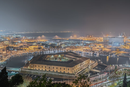Aerial view of the illuminated Lazzaretto di Ancona in the harbor at night with boats and industrial port infrastructure in Ancona, Marche, Italy.