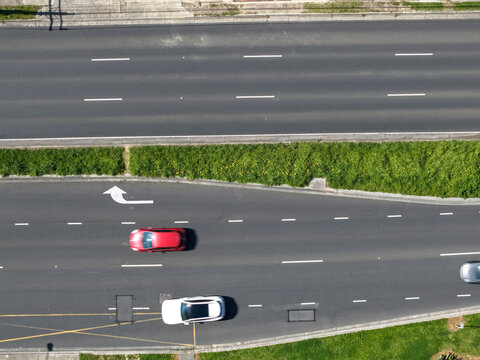Aerial view of a multi-lane road with a red car and a white car driving on the asphalt, surrounded by green grass verges in Melbourne, VIC, Australia.