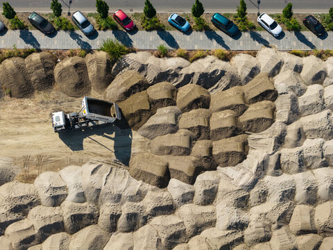 Aerial view of a dump truck unloading sand at a construction site near K-District, with parked cars visible on the adjacent street in Belgrade, Grad Beograd, Serbia.