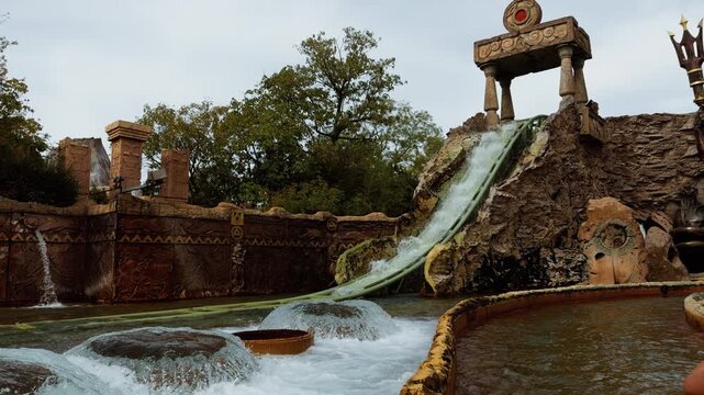 Water runs down a steep section of the Fuga da Atlantide ride at Gardaland in Italy. Temple style columns and rocky scenery surround the track.
