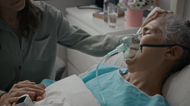 Adult woman comforting sick Caucasian senior female patient wearing oxygen mask and pulse oximeter. Footage suitable for healthcare campaigns, hospice care marketing, and medical insurance promos