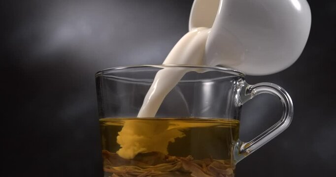 Milk pouring into green tea in glass cup slow motion black background