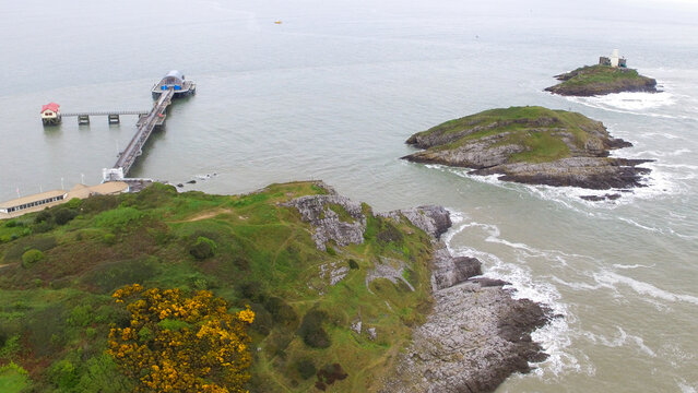 Aerial view of Mumbles Lighthouse situated on a rocky island near the Mumbles Pier, surrounded by the sea and green coastal cliffs in Mumbles, Wales, United Kingdom.