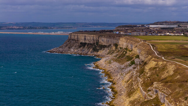 Aerial view of the dramatic limestone cliffs and coastal path of the Isle of Portland overlooking the sea in Portland, England, United Kingdom.