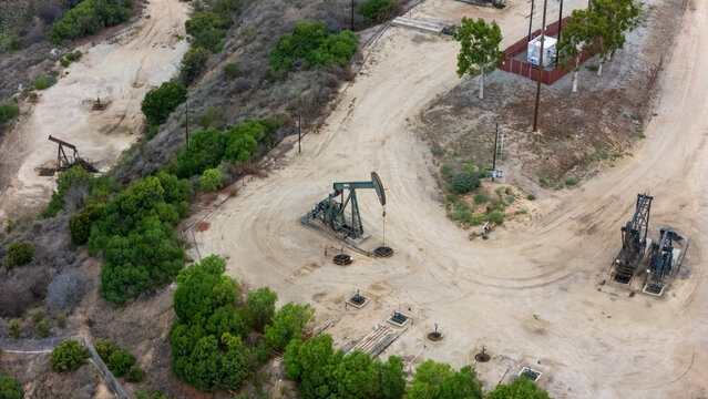 Aerial view of oil pumpjacks operating in the Baldwin Hills oil field with dirt access roads and surrounding vegetation in Los Angeles, California, United States.