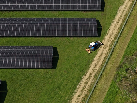 The Basin, Victoria, Australia - 18 September 2026: Aerial view of a solar farm with rows of photovoltaic panels arranged on green grass, featuring a blue tractor driving along a dirt path.