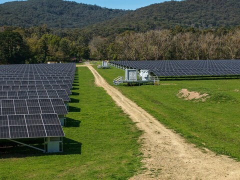 The Basin, Victoria, Australia - 18 September 2026: Aerial view of a solar farm with rows of photovoltaic panels in a grassy field, featuring a dirt path and rolling hills in the background.