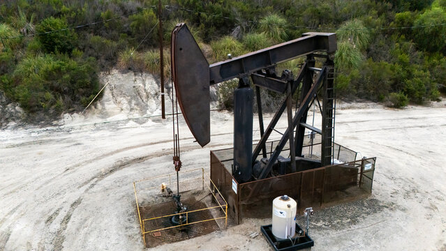 Inglewood, California, United States - 16 September 2026: Aerial view of an oil pump jack operating in a rural area with dirt ground and surrounding green vegetation.