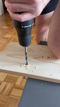Close-up of a person drilling a hole in a wooden board for an indoor home project