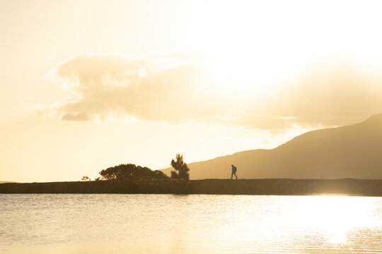 lone silhouette hiker at sunset walking nature path near water and mountains, Stanford, South Africa