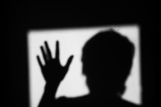 Close up black and white shadow of man showing palm hand waving gesture on the wall