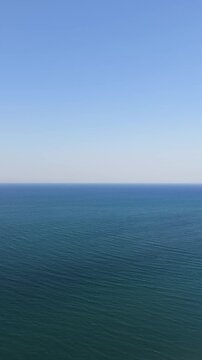 Vertical aerial drone shot of endless deep blue sea water meeting clear sky at the distant horizon line offering minimal copy space for social media