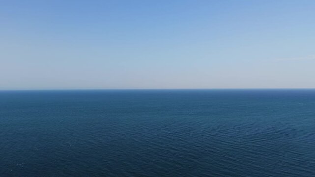 Wide aerial drone shot of open deep blue sea water meeting clear sky at the distant horizon on a calm summer day