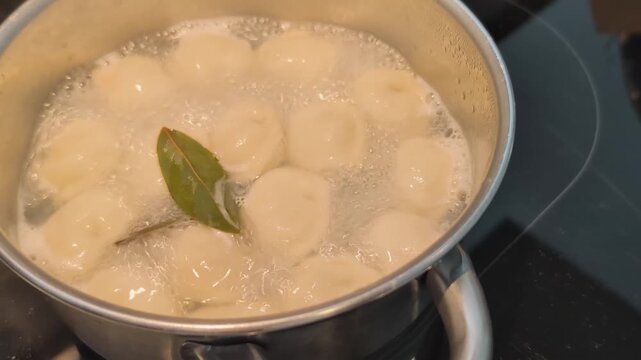 Boiling pelmeni or ravioli with bay leaf in a pot on the stove