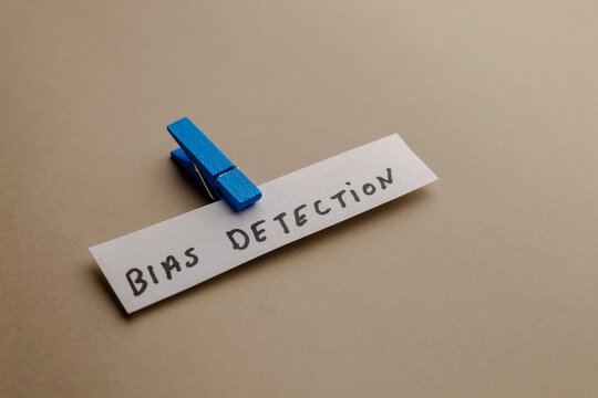 A paper strip with the text bias detection written in marker and held by a blue wooden clothespin against a neutral beige background tone