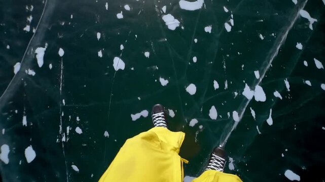 Skater man ice skating on frozen Baikal lake. Pov view guy legs in yellow pants moving across dark deep blue cracked ice, snowy edges. Winter active lifestyle travel exploration and freedom. Fun hobby
