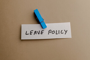 Obraz premium A close up view of a paper note with leave policy text handwritten in black ink attached by a wooden blue clothespin on a brown background