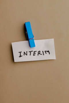 Interim text written on paper note attached with blue wooden peg on brown background for business temporary role concept and job position