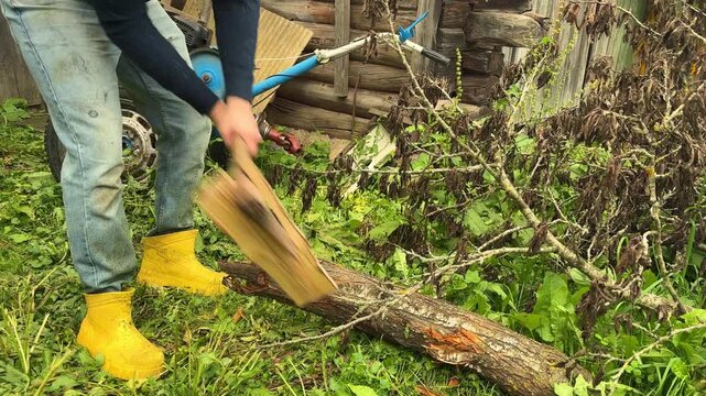 A man chops a log with an axe in a rural yard, outdoor labor, household work, firewood preparation.