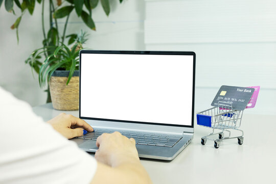 Blank white screen computer, credit card and mini shopping cart on table. Online shopping concept. Laptop mock up screen view.
