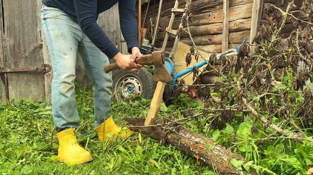 A man splits firewood with an axe in a grassy yard, rural labor, household chores, wood preparation.