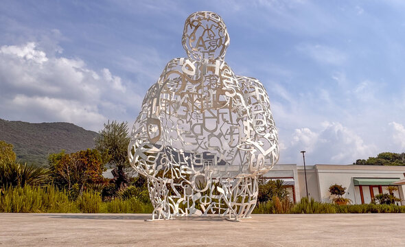 15.09.2026,Porto Montenegro.Large white human-shaped sculpture made from letters and symbols in Porto Montenegro, Tivat, standing against blue sky with landscaped greenery and mountains.