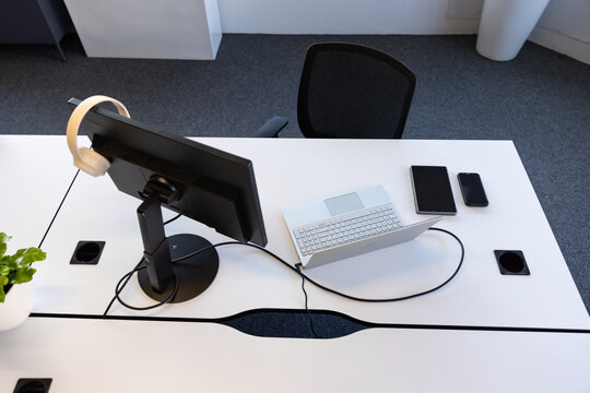 Workstation is featuring black monitor with headphones, white laptop and smartphone on bench desk