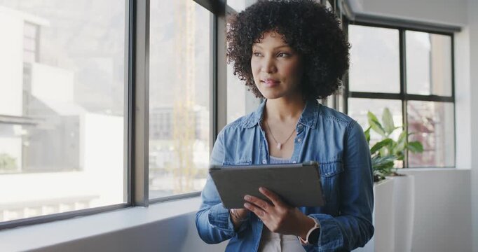African woman starting work tapping tablet checking mail then gazing at office window denim shirt