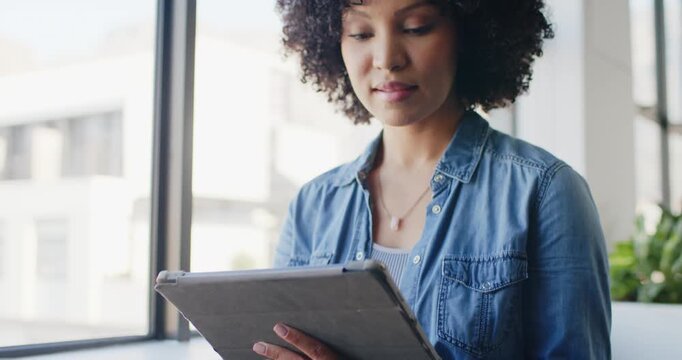 African American woman holding tablet, tapping, scrolling while reading at window with smartwatch